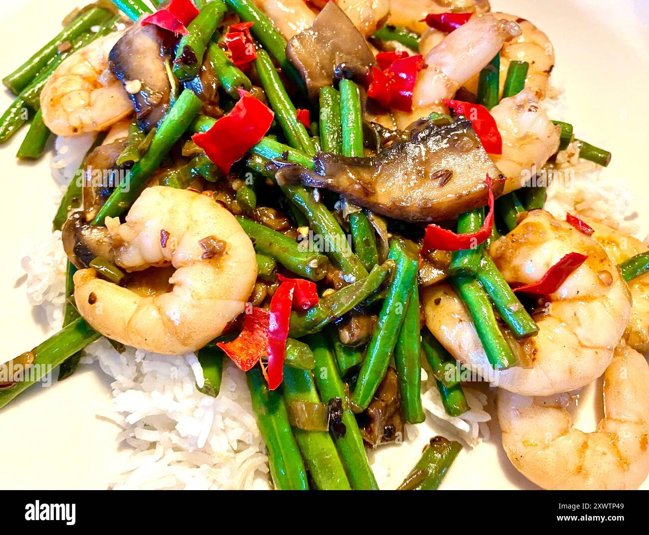 Crevettes asiatiques sautées, haricots verts et piments sur un lit de riz Banque D'Images