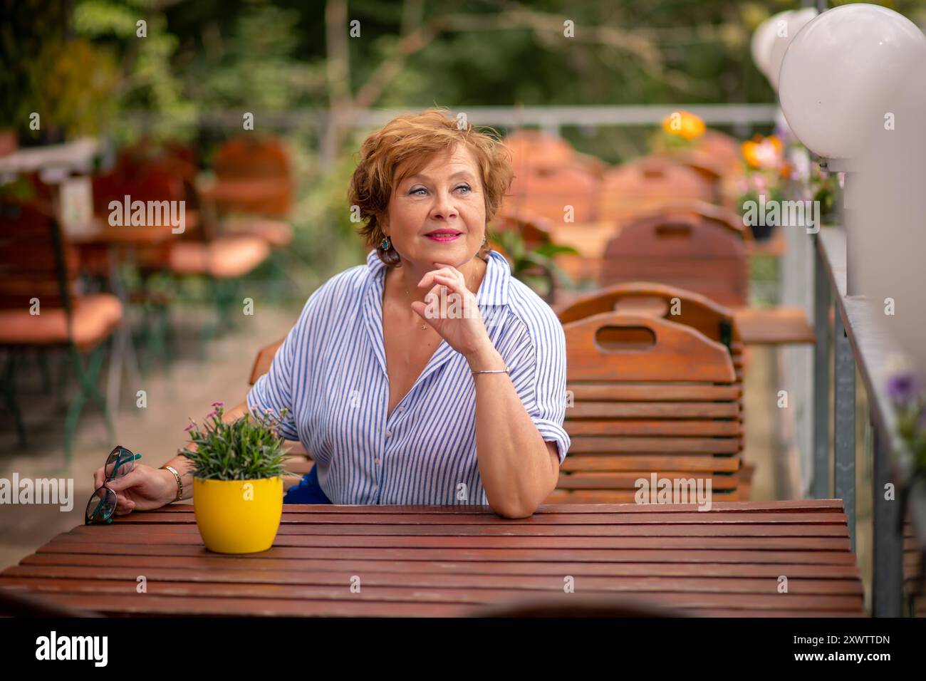 Une femme est assise à une table en bois, regardant soigneusement loin tout en tenant une plante en pot et en profitant de l'atmosphère sereine du café. Banque D'Images