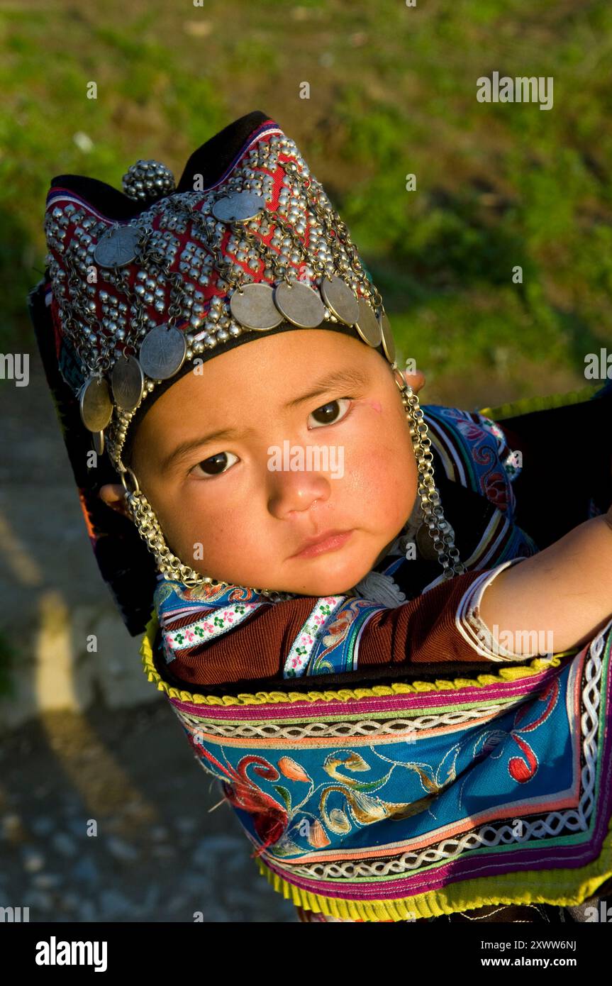 Un joli bébé Hani portant un chapeau traditionnel. Comté de Yuanyang, Yunnan, Chine. Banque D'Images