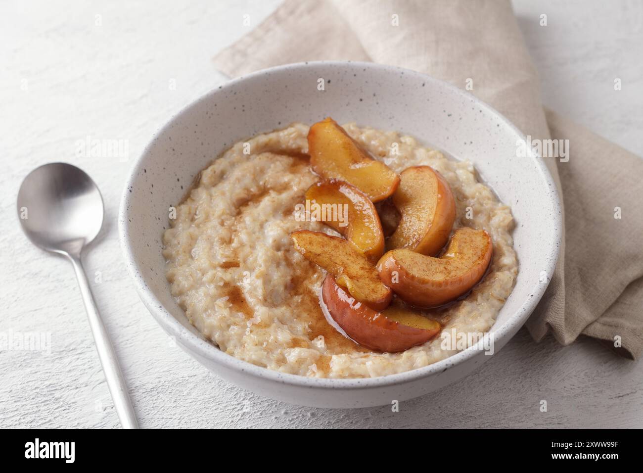 Bouillie d'avoine sucrée avec tranches de pomme cuites au four, cannelle et sauce caramel dans un bol gris sur un fond clair, vue de dessus. Délicieuse cuisine maison Banque D'Images