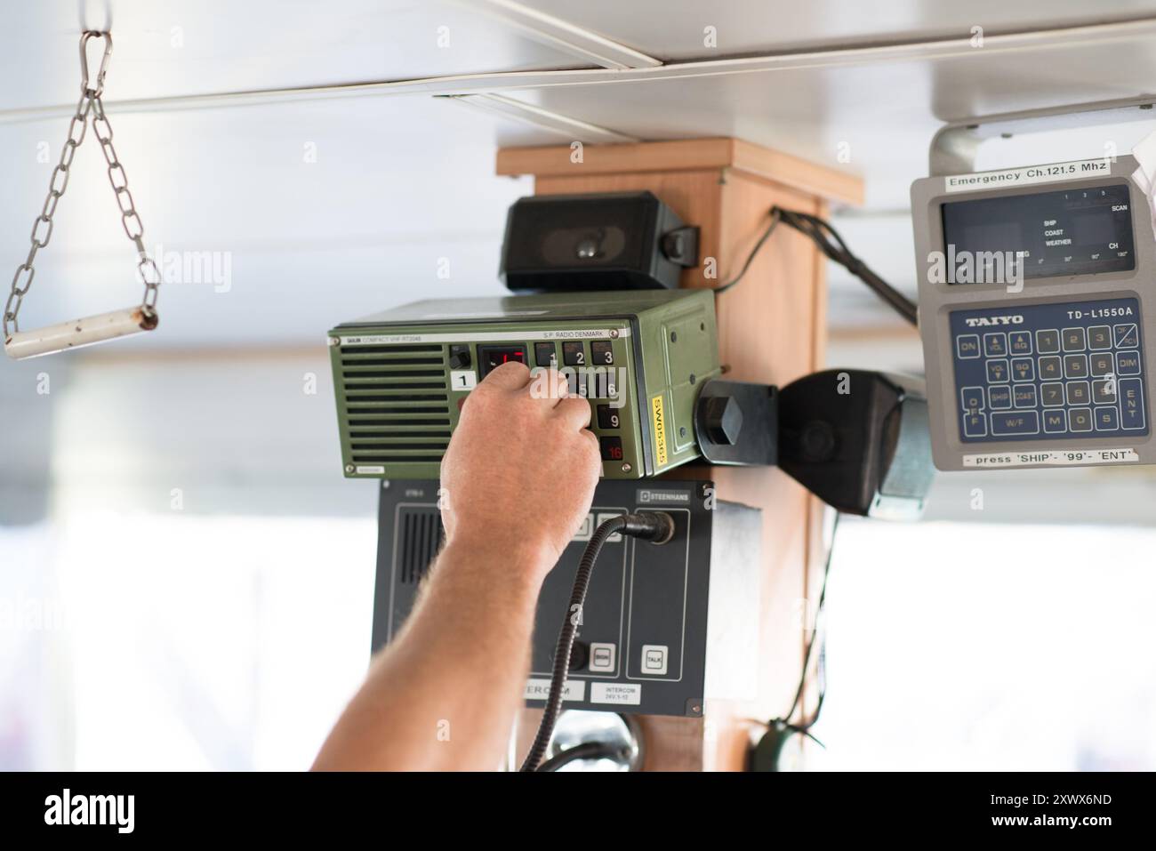 Vue rapprochée d'une main actionnant un panneau de commande radio de communication à l'intérieur d'un navire. L'image met en évidence la technologie maritime utilisée dans la navigation et la sécurité. Essentiel pour la communication maritime et la gestion des urgences. Banque D'Images