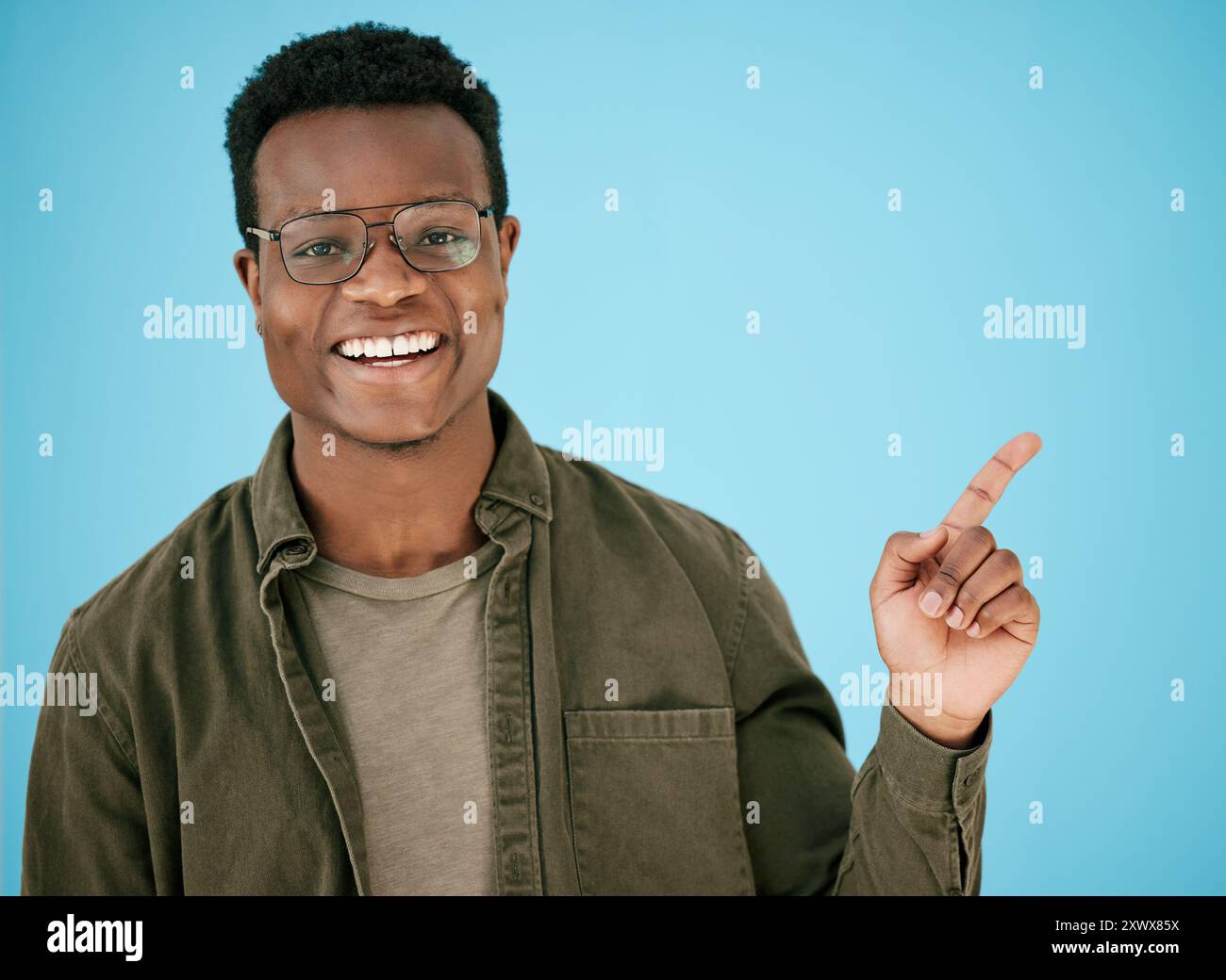 Pointage, portrait et sourire avec l'homme noir sur fond bleu en studio pour l'annonce ou la promotion. Visage, lunettes et marketing avec personne heureuse Banque D'Images