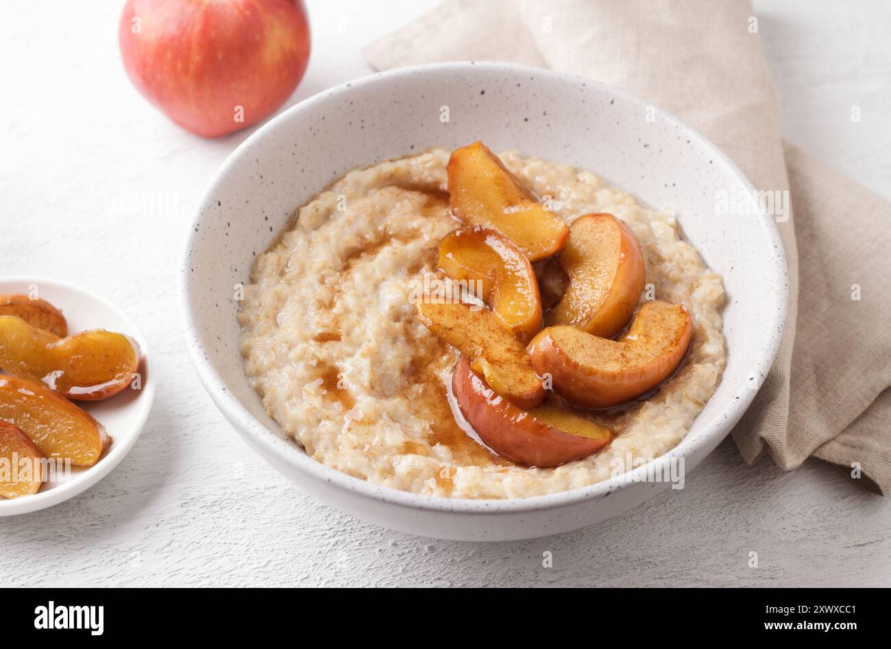 Bouillie d'avoine sucrée avec tranches de pomme cuites au four, cannelle et sauce caramel dans un bol gris sur un fond clair, vue de dessus. Délicieuse cuisine maison Banque D'Images
