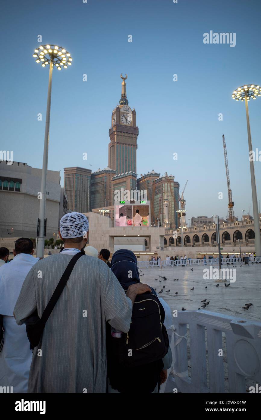 La Mecque, Arabie Saoudite - 5 juin 2024 : un couple de pèlerins du Hadj et de l'Umrah marchant près de Masjidil Haram, Grande Mosquée de la Mecque, avec une tour de l'horloge dans la BA Banque D'Images