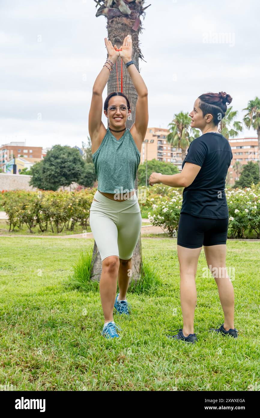 Deux femmes font de l'exercice dans un parc en utilisant des bandes de résistance pour tonifier leurs muscles et améliorer leur endurance physique, profitant d'un environnement vert et frais Banque D'Images