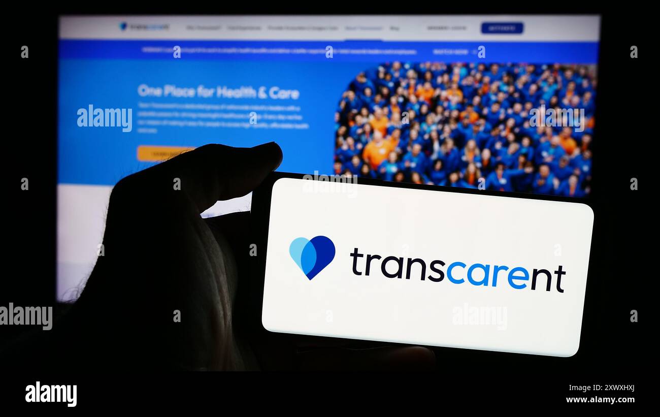 Personne tenant le téléphone portable avec le logo de la société américaine de soins de santé Transcarent Inc en face de la page Web de l'entreprise. Concentrez-vous sur l'affichage du téléphone. Banque D'Images