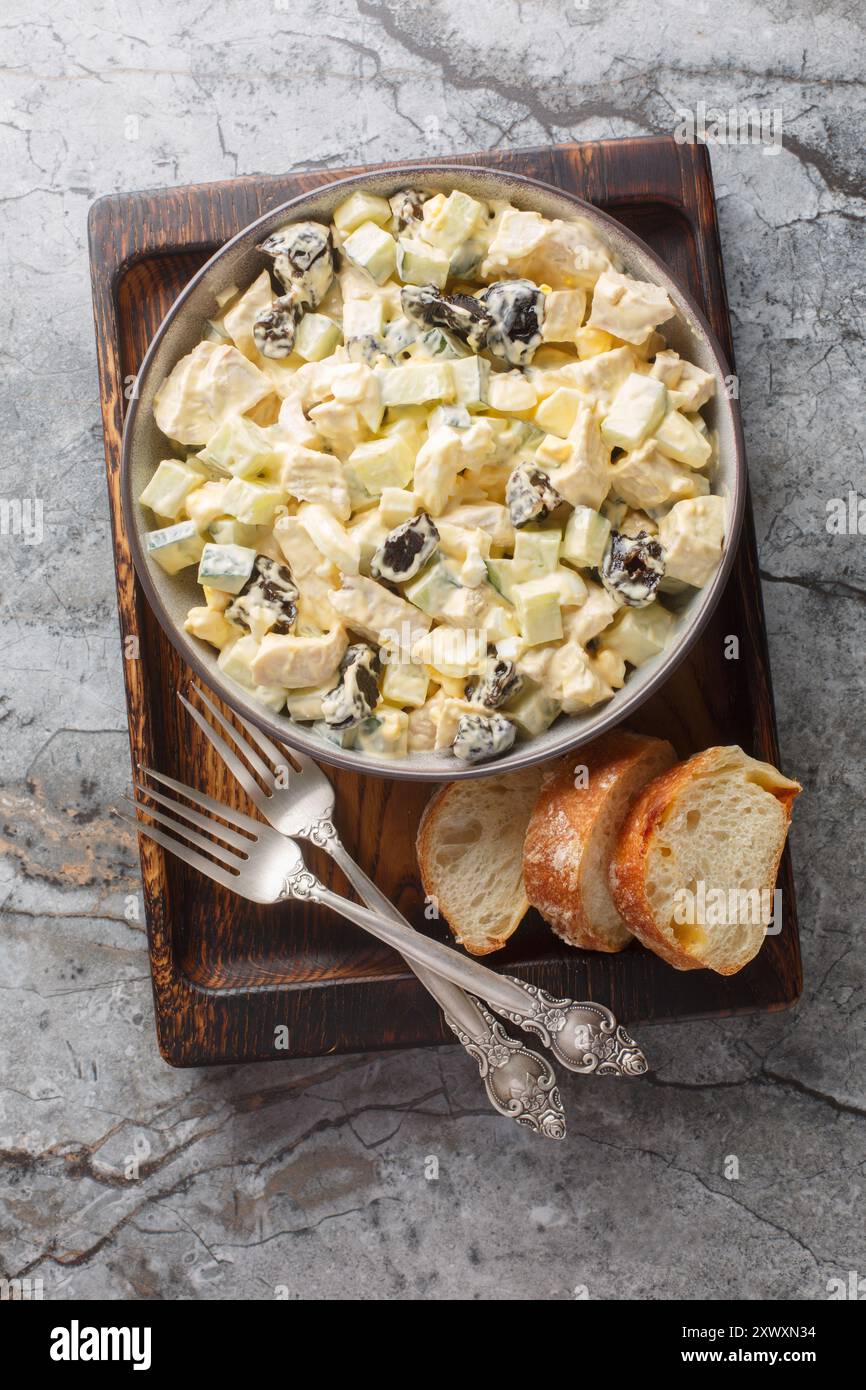 Salade avec poulet, pruneaux, œufs durs et concombre frais habillé de mayonnaise gros plan dans un bol sur une planche de bois. Vue de dessus verticale Banque D'Images