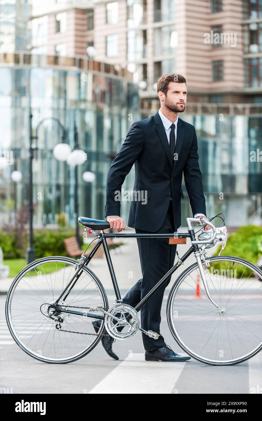 Homme d'affaires avec vélo. Toute la longueur du beau jeune homme d'affaires roulant son vélo tout en traversant la route Banque D'Images