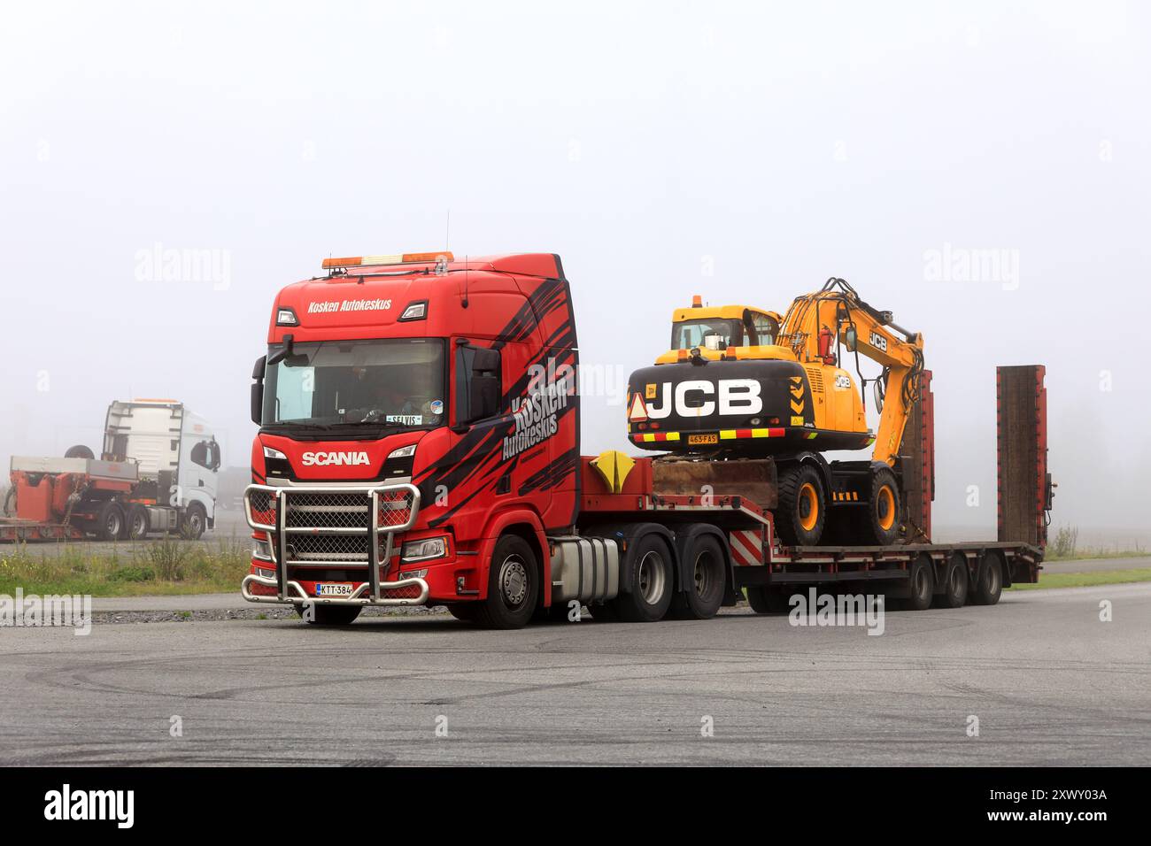 Remorque Red Scania Truck Drop Deck garée sur une cour un matin brumeux prêt à transporter JCB JS145W excavatrice sur roues. Forssa, Finlande. 8 août 2024. Banque D'Images