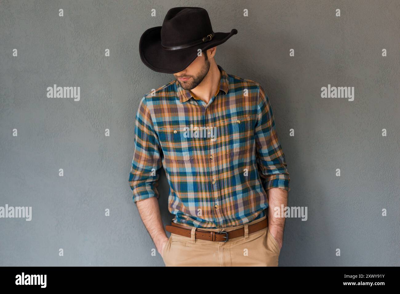 Couture cow-boy. Portrait d'un jeune homme portant un chapeau de cow-boy et regardant vers le bas tout en se tenant debout sur fond gris Banque D'Images