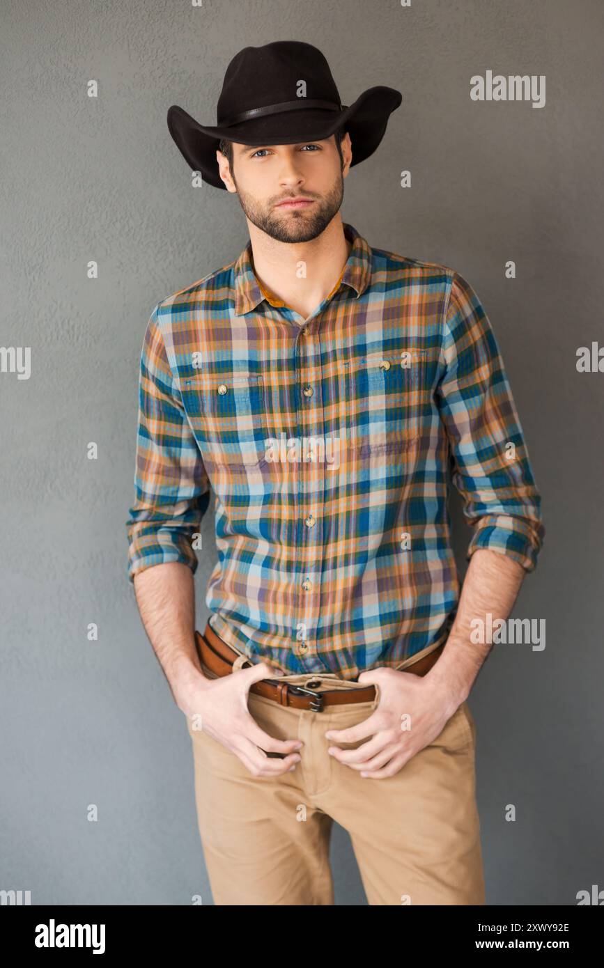 Brave cow-boy. Beau jeune homme portant un chapeau de cow-boy et regardant la caméra tout en se tenant debout sur fond gris Banque D'Images