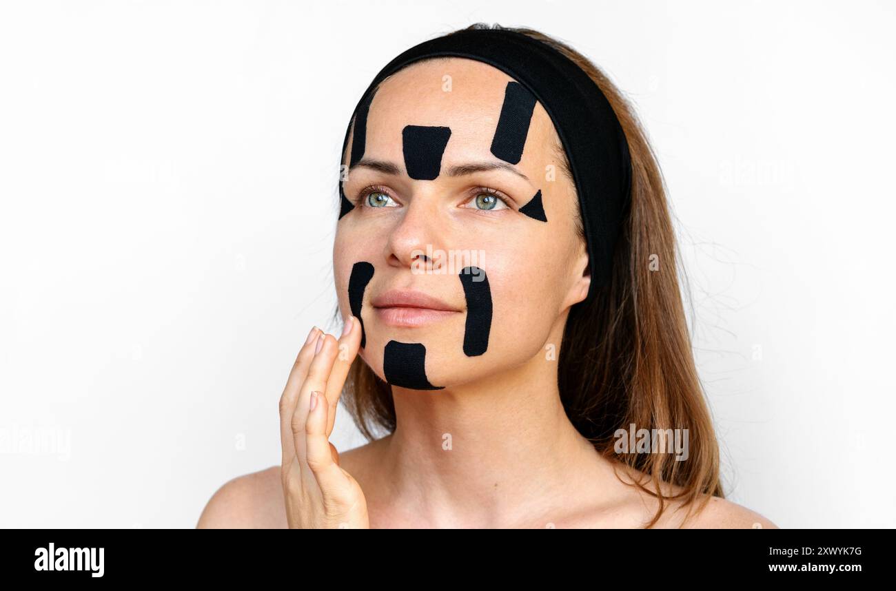 Jeune femme modèle de beauté applique des bandes faciales de couleur noire sur son visage. Banque D'Images