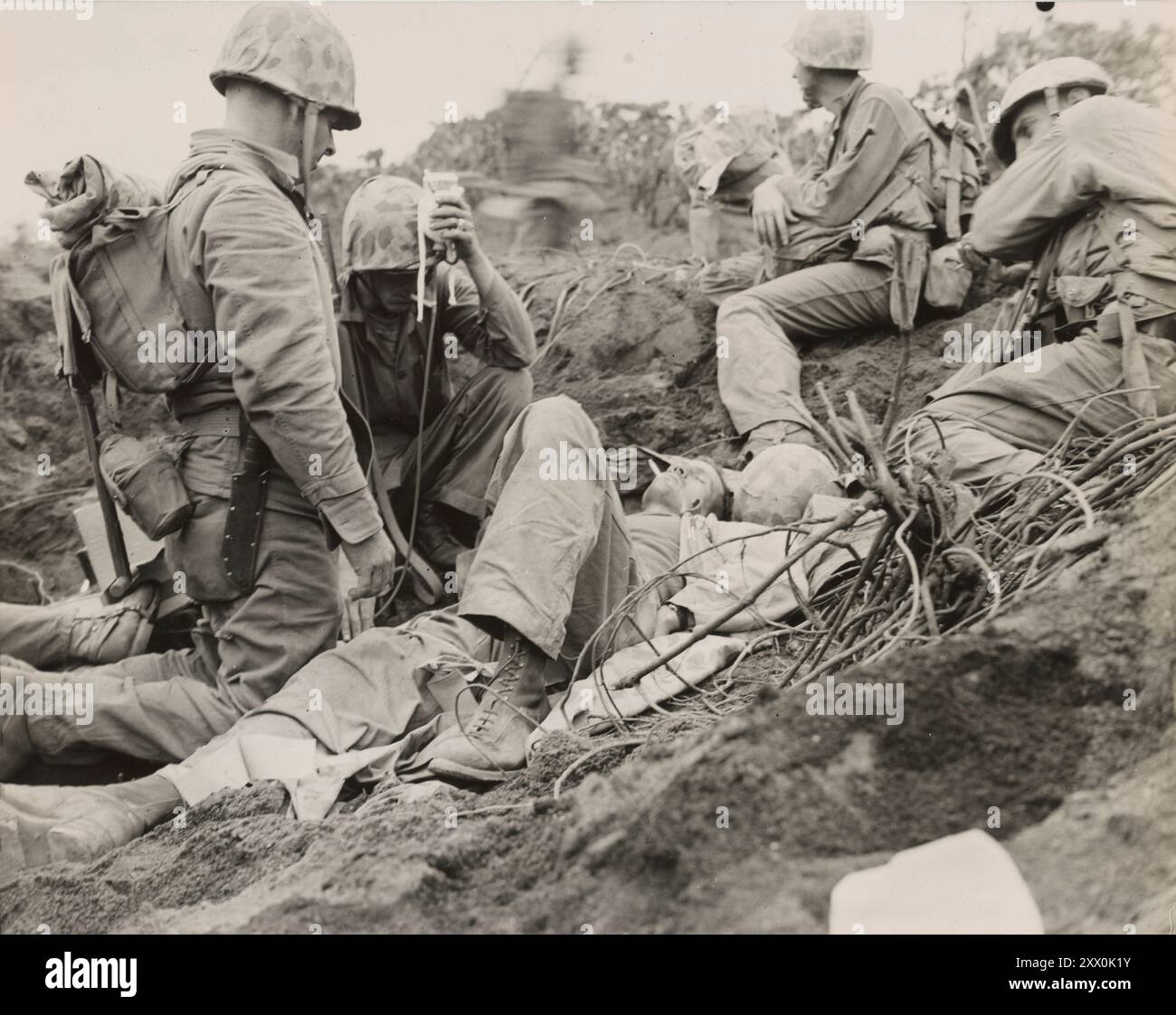 Bataille d'Iwo Jima (19 février – 26 mars 1945). Une cigarette et du plasma... Avec des marines l'aidant, un corps de la Navy donne un plasma de sang marin blessé entre la piste d'atterrissage numéro deux de Motoyama et Purple Beach le jour J plus trois, la victime gagne un peu de plaisir avec une cigarette. Jwo Jime, Japon Banque D'Images