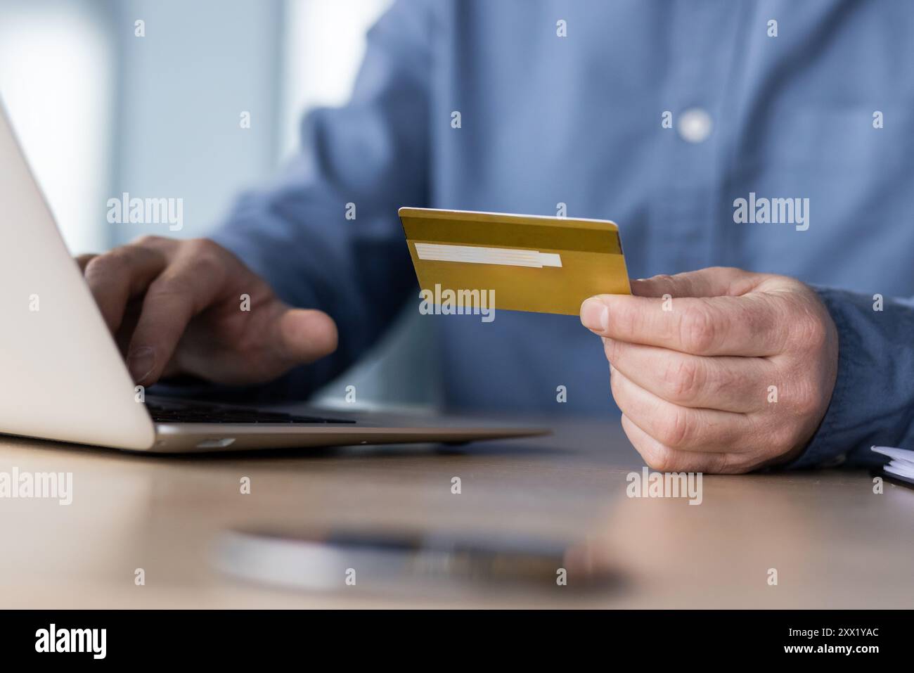Photo en gros plan d'une partie du corps, jeunes mains d'un homme en chemise bleue assis à une table, tenant une carte de crédit et tapant sur un clavier d'ordinateur portable. Banque D'Images