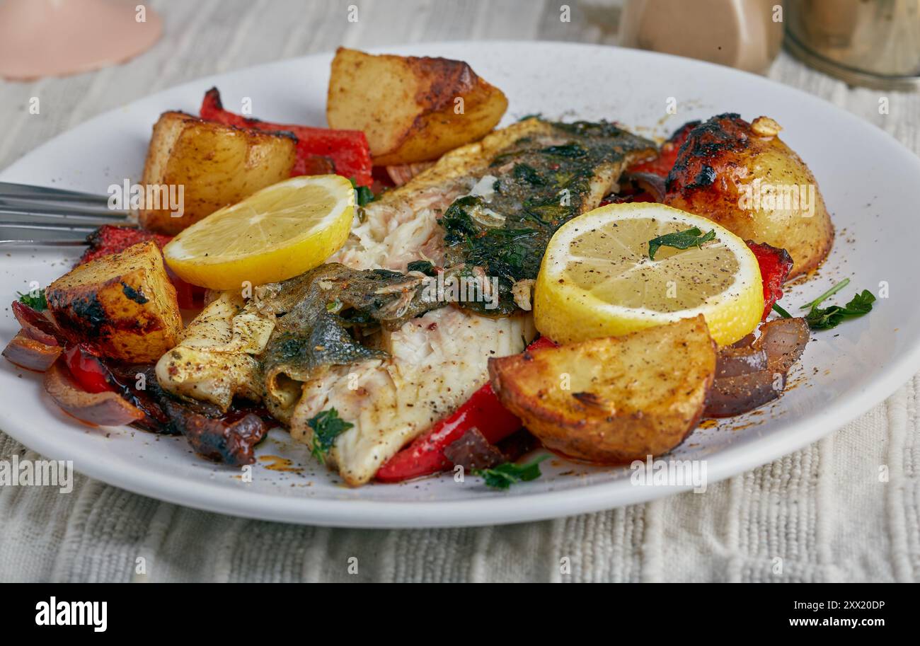 Filet de poisson cuit à la poêle avec des légumes rôtis et garni de tranches de citron. Banque D'Images