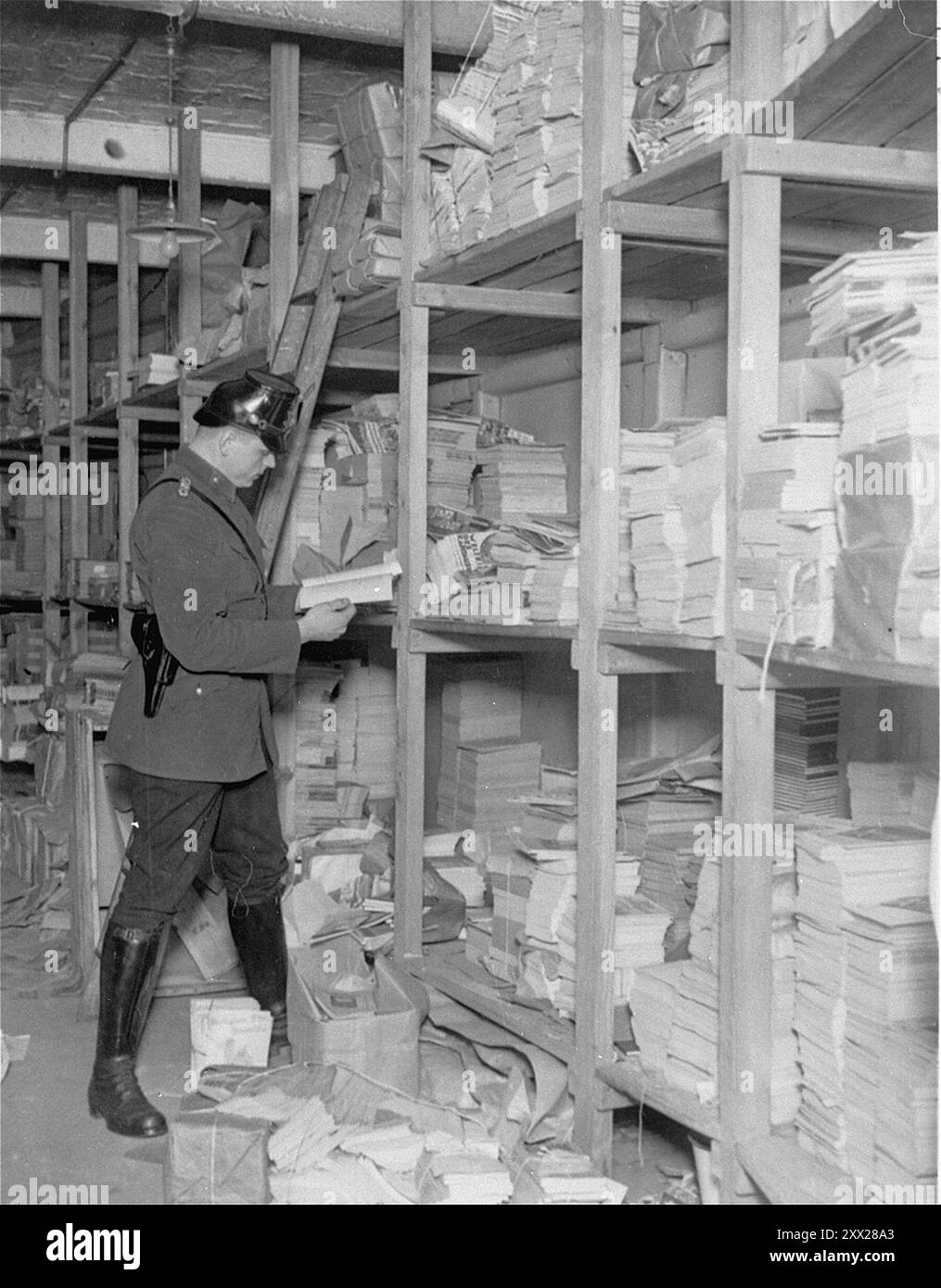 Un membre de la Schutzpolizei examine les publications dans un entrepôt lors de la fermeture de la maison Karl-Liebknecht (siège du KPD), qui se trouvait sur la Buelowplatz à Berlin. Après que Hitler eut reçu le pouvoir, il se déplaça rapidement et efficacement pour le garder. Après l'incendie du Reichstag, les communistes ont été blâmés (qui a effectivement mis le feu est encore dans le doute). Après une campagne anti-comuniste frénétique, ils ont été déclarés illégaux, les membres ont été emprisonnés, leurs bureaux ont été saccagés et toute la littérature détruite. Avec l'opposition affective ainsi éliminée, les nazis remportèrent facilement les élections générales un mois plus tard. Banque D'Images