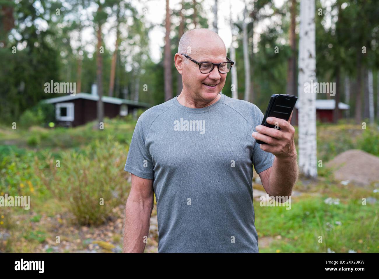 Homme finlandais senior utilisant le téléphone portable à l'extérieur dans un été de forêt scandinave en Finlande concept Banque D'Images