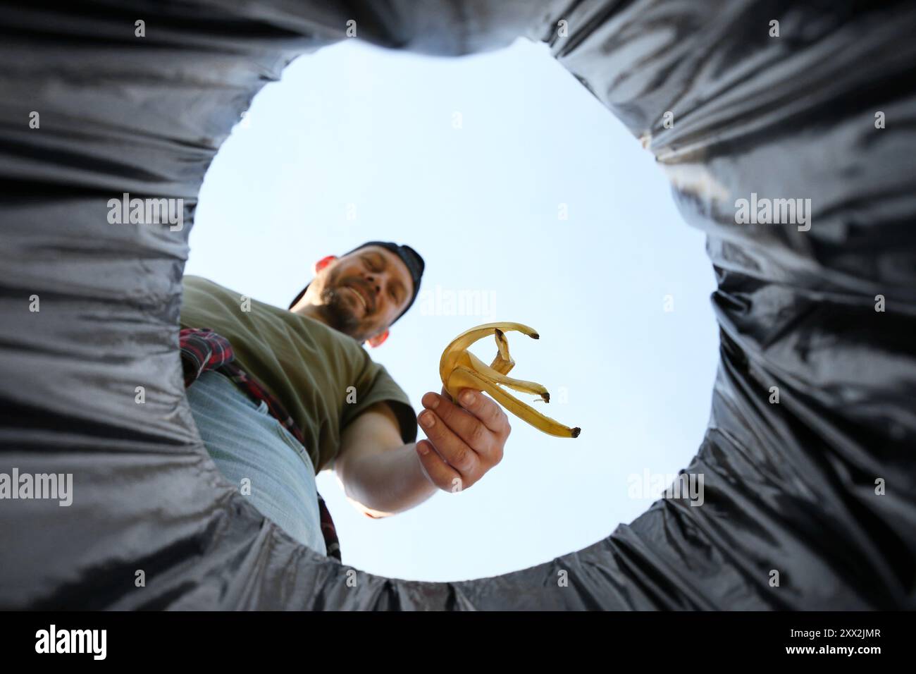 Homme jetant de la peau de banane dans la poubelle à l'extérieur, vue de dessous Banque D'Images