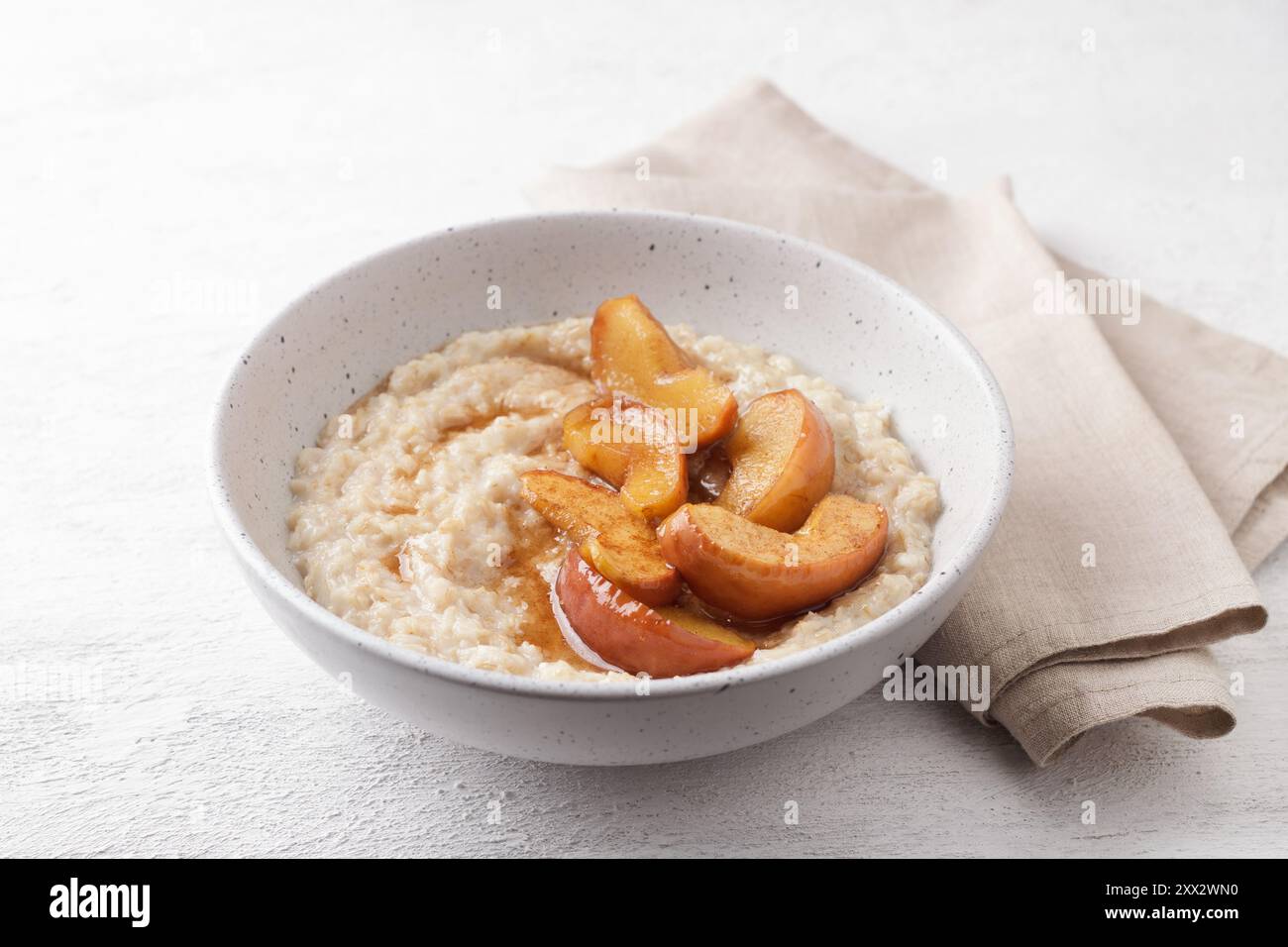 Bouillie d'avoine sucrée avec tranches de pomme cuites au four, cannelle et sauce caramel dans un bol gris sur un fond clair, vue de dessus. Délicieuse cuisine maison Banque D'Images