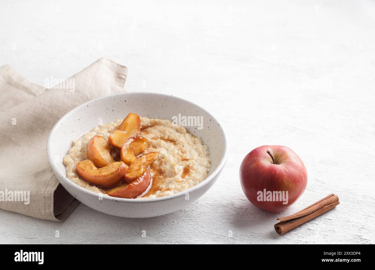 Bouillie d'avoine sucrée avec tranches de pomme cuites au four, cannelle et sauce caramel dans un bol gris sur fond clair Banque D'Images