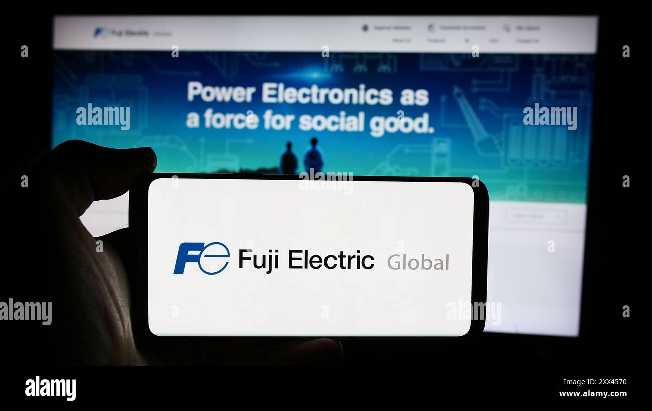 Personne tenant le téléphone portable avec le logo de la société japonaise Fuji Electric Co. Ltd devant la page Web de l'entreprise. Concentrez-vous sur l'affichage du téléphone. Banque D'Images