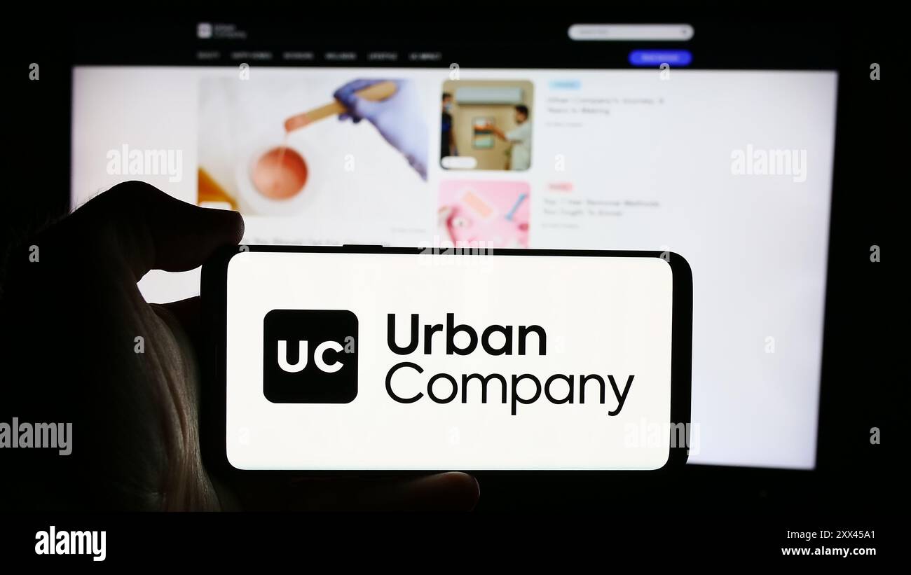 Personne tenant le téléphone portable avec le logo de la société indienne de marché de services à domicile Urban Company en face de la page Web. Concentrez-vous sur l'affichage du téléphone. Banque D'Images