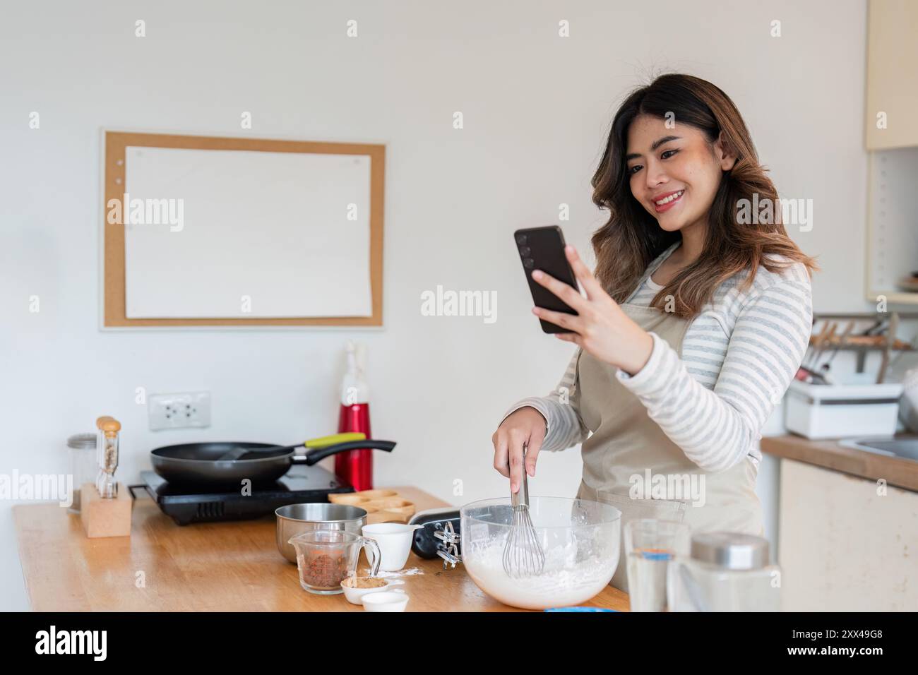 Femme apprenant la cuisson en ligne, exploration culinaire dans la cuisine moderne Banque D'Images