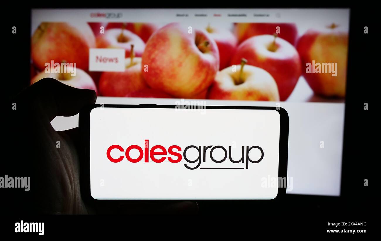 Personne tenant le téléphone portable avec le logo de la société australienne de vente au détail Coles Group Limited devant la page Web de l'entreprise. Concentrez-vous sur l'affichage du téléphone. Banque D'Images