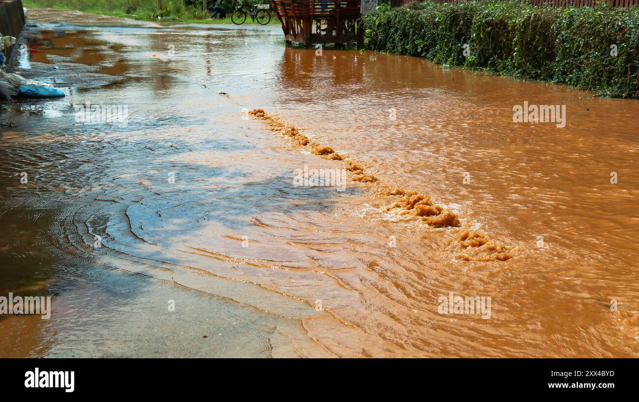 Une image puissante d'une épaisse inondation rouge s'infiltrant à travers les fissures d'une route, mettant en évidence la force destructrice des inondations sur les infrastructures. Banque D'Images