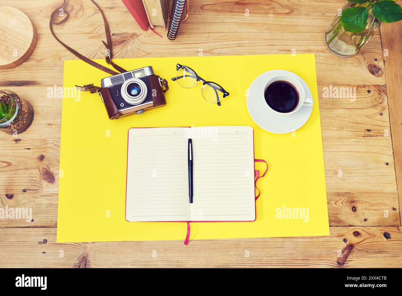 Ordinateur portable, appareil photo et au-dessus avec café pour un espace de travail créatif, art ou design sur le bureau. Vue de dessus de l'espace vide avec livre, affiche jaune et stylo pour Banque D'Images