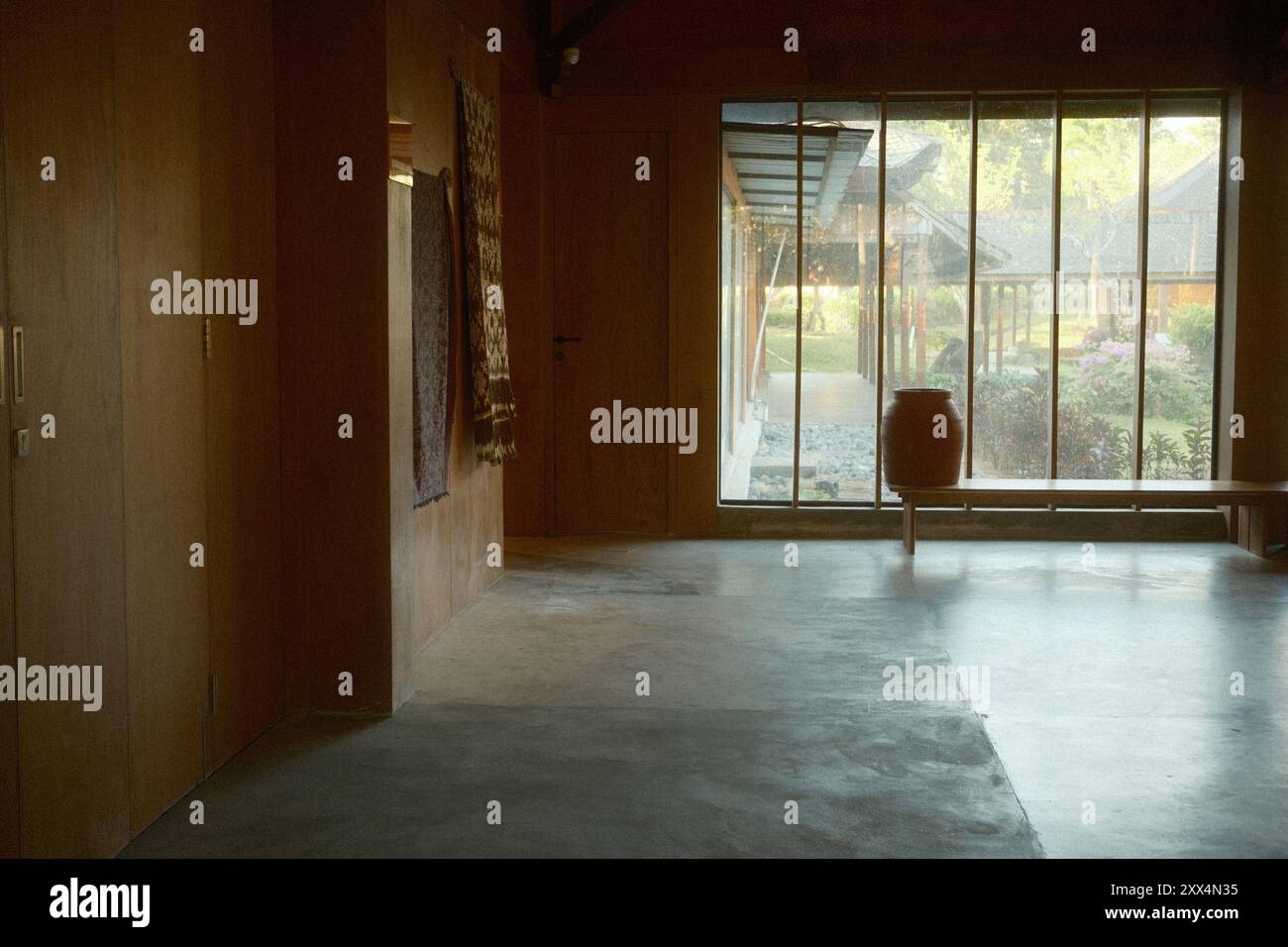 Un espace intérieur de style japonais avec des sols en béton, de grandes fenêtres en verre, des murs en bois et une vue sur le jardin Banque D'Images
