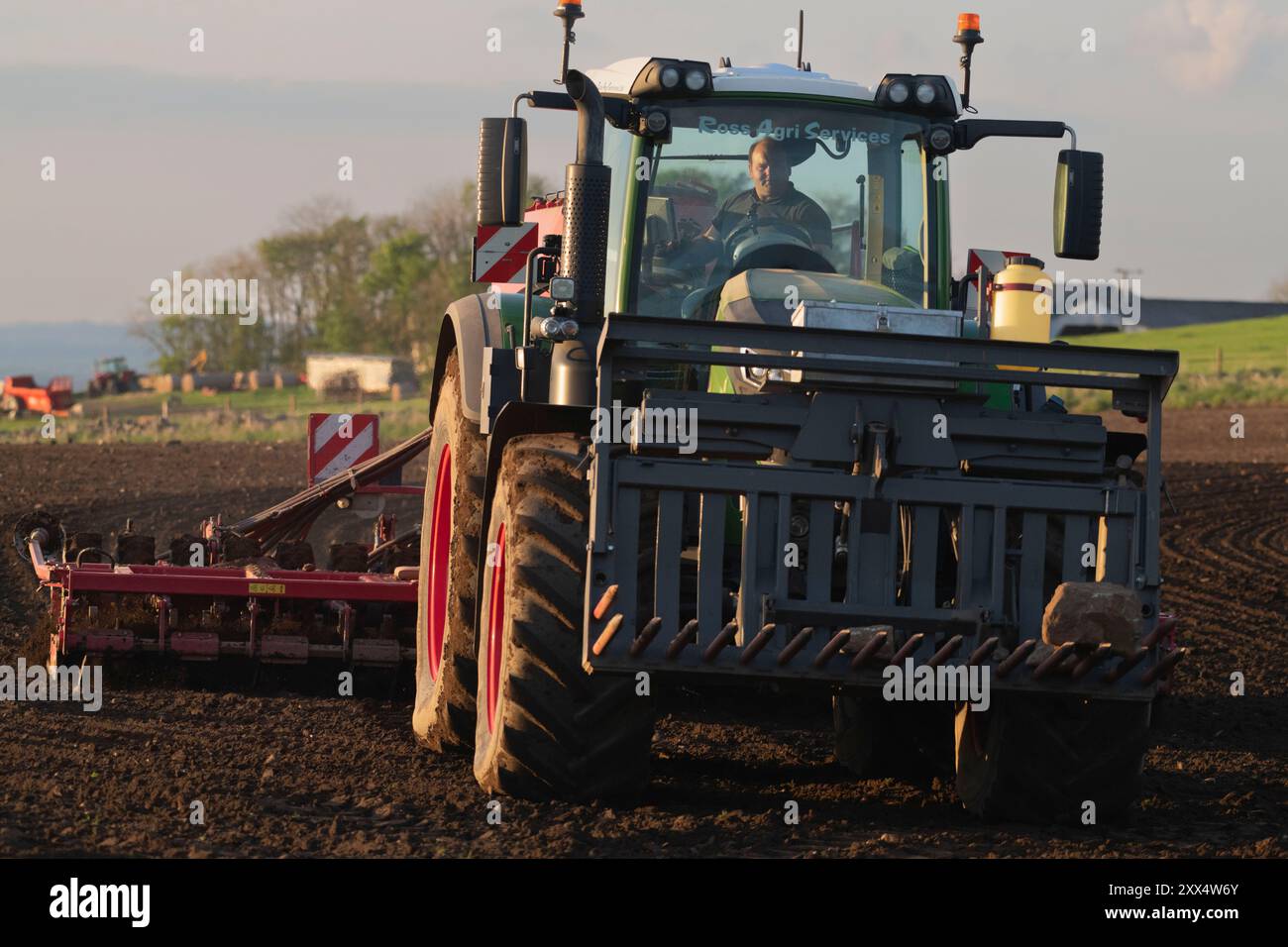 Vue de face d'un tracteur Fendt vert semant de l'orge avec un semoir à disques dans un champ labouré au soleil du soir Banque D'Images