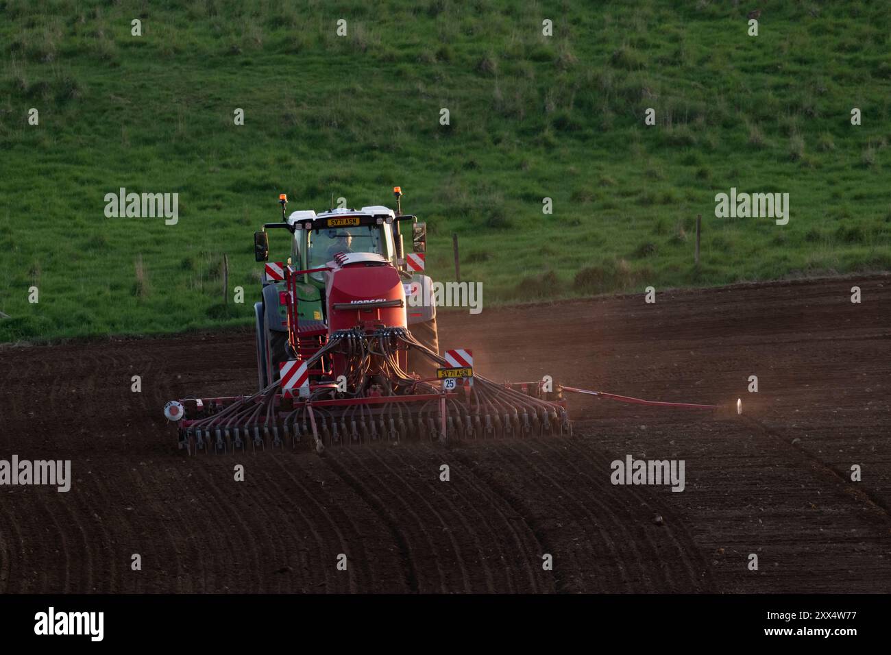 Vue arrière d'un tracteur Fendt équipé d'un semoir à disque Horsch semant un champ avec de l'orge tard dans la soirée au printemps Banque D'Images