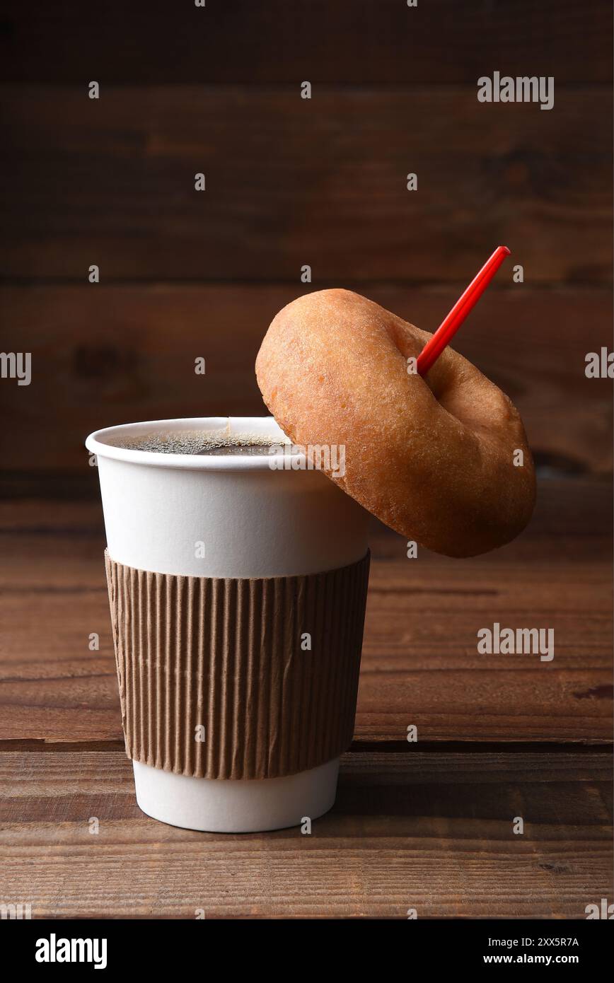 Gros plan d'une tasse en papier de café chaud fraîchement infusé avec une cuillère rouge, Un beignet simple à l'ancienne est suspendu à la cuillère. Format vertical avec copie spa Banque D'Images