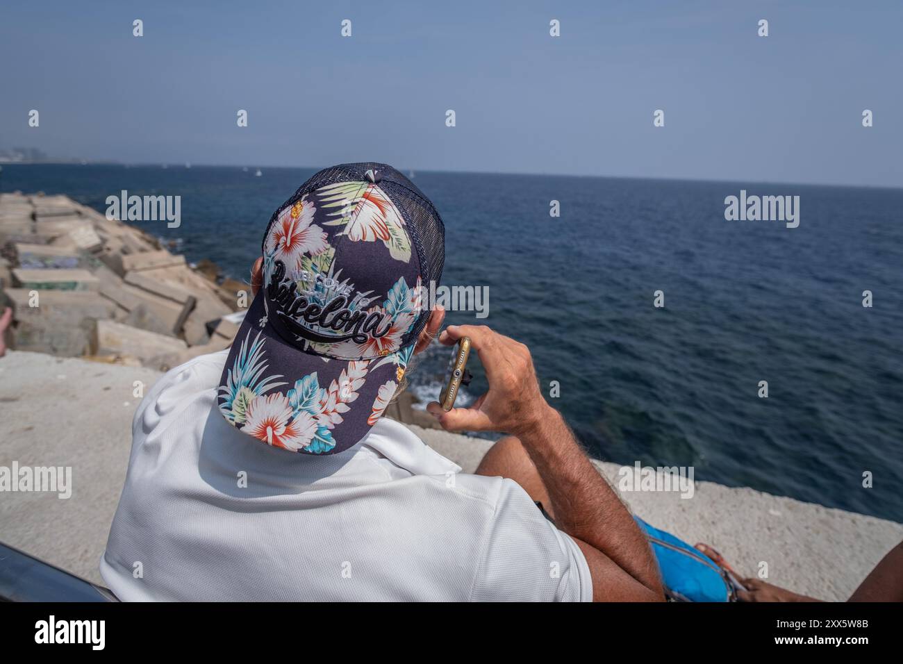 Barcelone, Espagne. 22 août 2024. Un spectateur portant une casquette avec le texte Wellcome Barcelona est vu sur la jetée suite aux régates sur son téléphone portable. La Louis Vuitton Preliminary Regatta 2024 America's Cup a entamé les premières courses préliminaires ce matin. Visiteurs, touristes et résidents ont pu profiter gratuitement de la première course de la compétition depuis les points de vue sur le front de mer et sur de grands écrans situés dans les zones de fans. Crédit : SOPA images Limited/Alamy Live News Banque D'Images