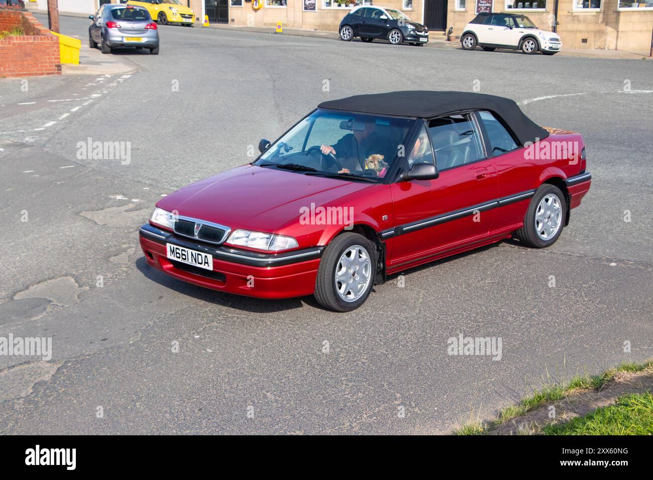 Une voiture rouge vintage Rover cabriolet conduisant dans une rue avec un homme derrière le volant, des bâtiments et d'autres voitures sont visibles en arrière-plan. Banque D'Images