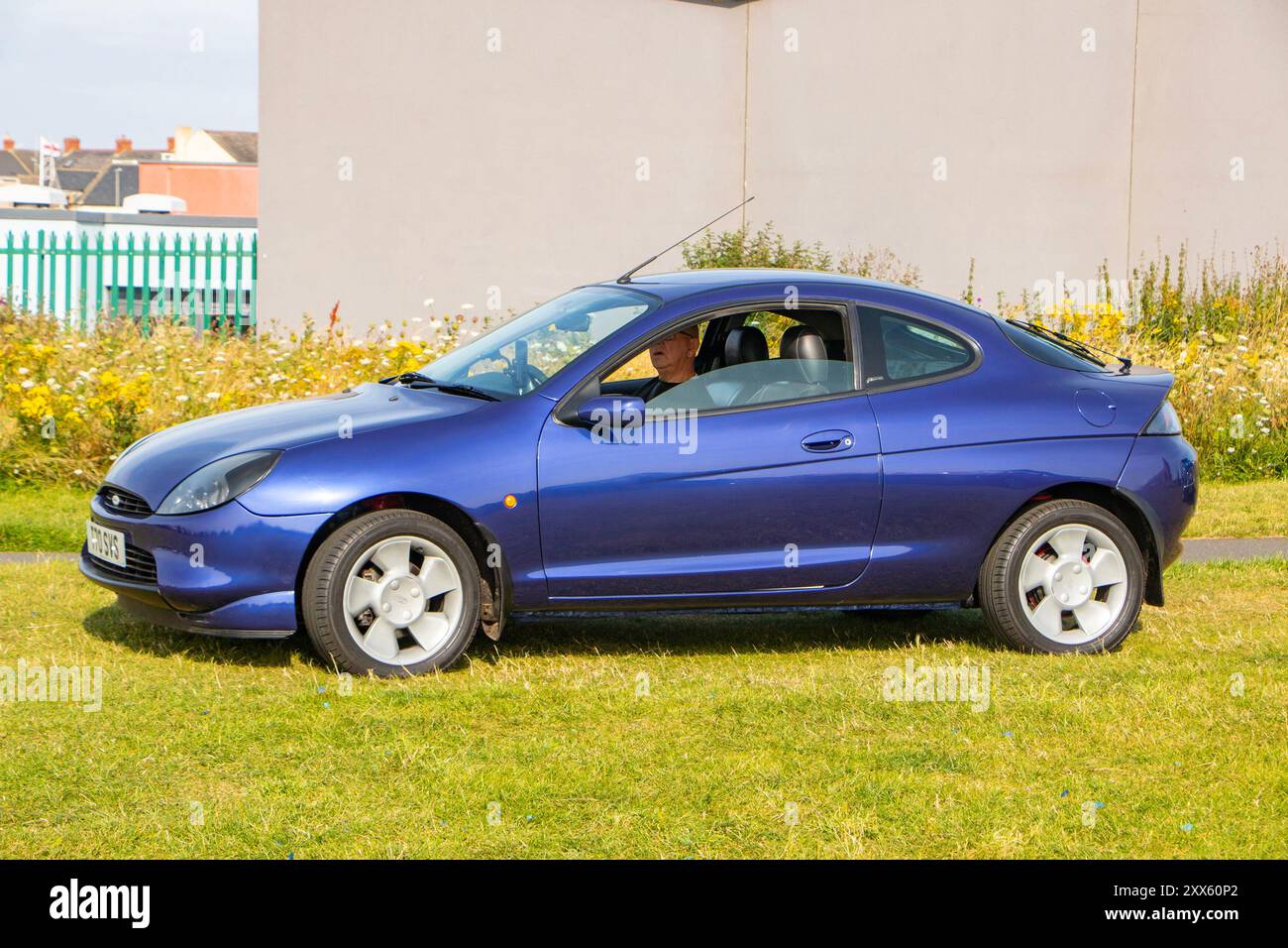 Un coupé Ford puma compact bleu garé sur une zone herbeuse près d'un bâtiment. Banque D'Images