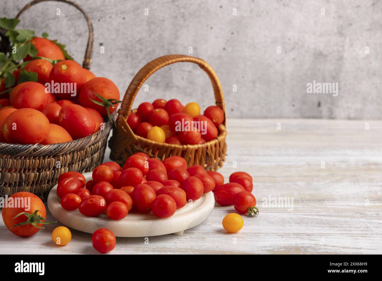 Tomates fraîches grandes et petites dans des paniers et sur un plateau blanc sur une table en bois Banque D'Images