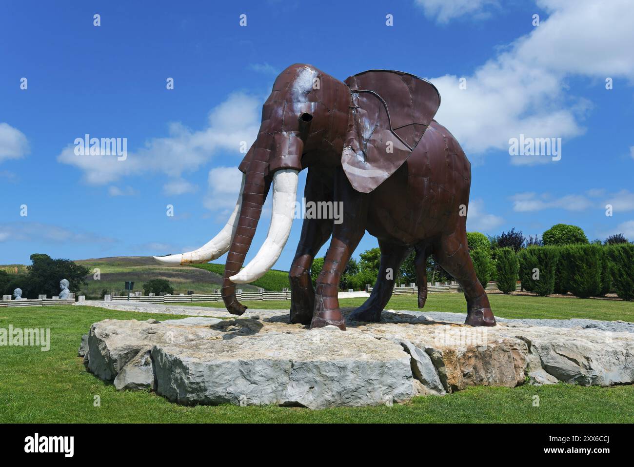 Sculpture en métal d'un éléphant sur une fondation rocheuse dans un parc vert sous un ciel bleu avec des nuages blancs, Bacalhoa, Bacalhoa Buddha Eden, Quinta dos Lo Banque D'Images