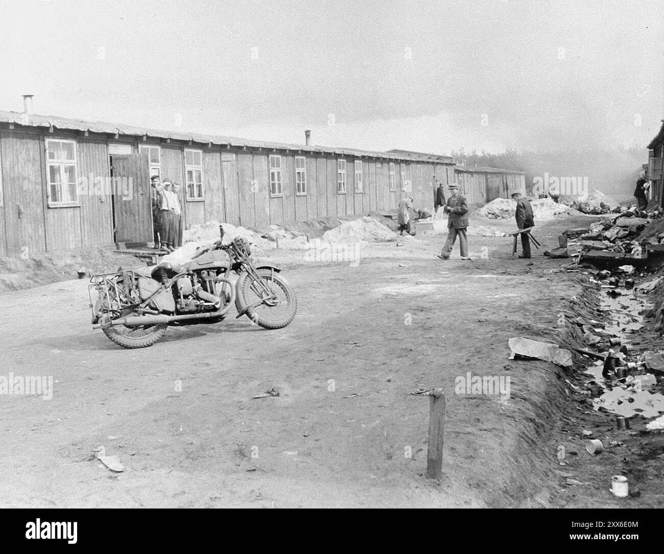 Une moto de l'armée et quelques survivants dans une rue du camp de concentration de Bergen-Belsen. La position du camp dans l'ouest de l'Allemagne signifiait que des milliers de personnes y furent envoyées alors que l'est tombait. 18000 personnes sont mortes rien qu'en mars 1945, et 10000 dans les deux semaines qui ont suivi la libération. Ils sont morts de maladie et de négligence plutôt que des abus systématiques observés ailleurs. Banque D'Images