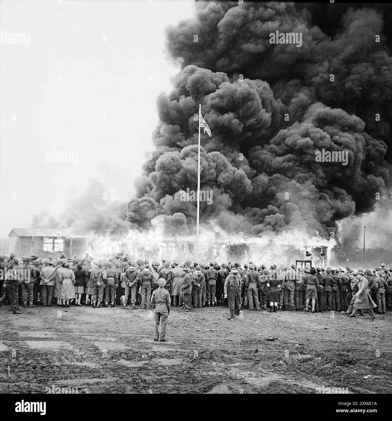 Une foule de prisonniers libérés du camp de concentration bergen Belsen regardant la dernière cabane brûler. Les conditions étaient si sordides et les maladies sévissaient que dès que possible les prisonniers étaient évacués et le camp détruit. La position du camp dans l'ouest de l'Allemagne signifiait que des milliers de personnes y furent envoyées alors que l'est tombait. 18000 personnes sont mortes rien qu'en mars 1945, et 10000 dans les deux semaines qui ont suivi la libération. Ils sont morts de maladie et de négligence plutôt que des abus systématiques observés ailleurs. Banque D'Images