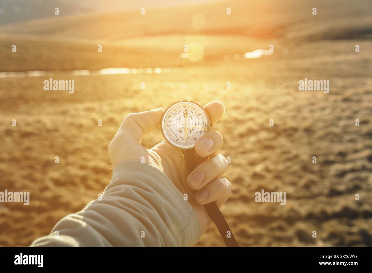 La main d'un homme tient une boussole à main sur fond de montagnes et de collines au coucher du soleil. Le concept de voyage et de navigation dans les espaces ouverts Banque D'Images