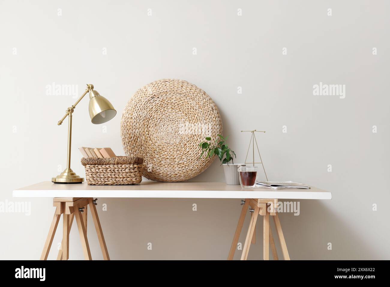 Table avec livres, tasse de thé, plante d'intérieur et lampe de bureau près du mur blanc Banque D'Images