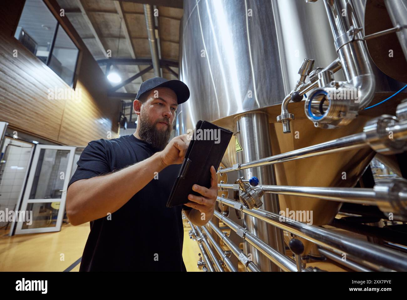 Homme, technologue avec la tablette en main vérifiant le système de brassage, s'assurant que chaque étape du processus répond à des normes de qualité strictes. Banque D'Images