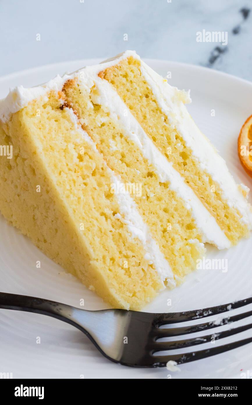 Tranche de gâteau en couches aromatisé à l'orange avec glaçage blanc sur une assiette Banque D'Images