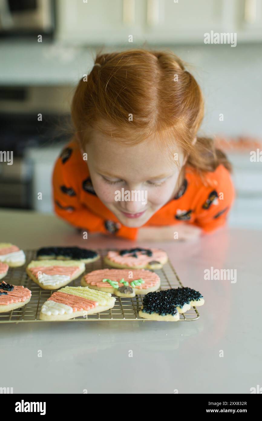 Fille aux cheveux rouges admirant des biscuits d'Halloween fraîchement décorés sur Banque D'Images