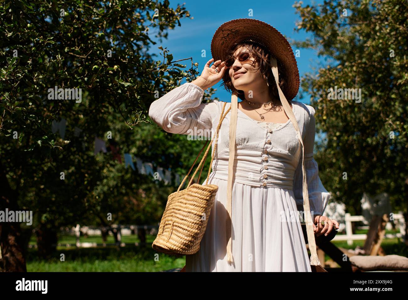 Une jeune femme en robe blanche et chapeau de paille sourit dans un jardin d'été. Banque D'Images