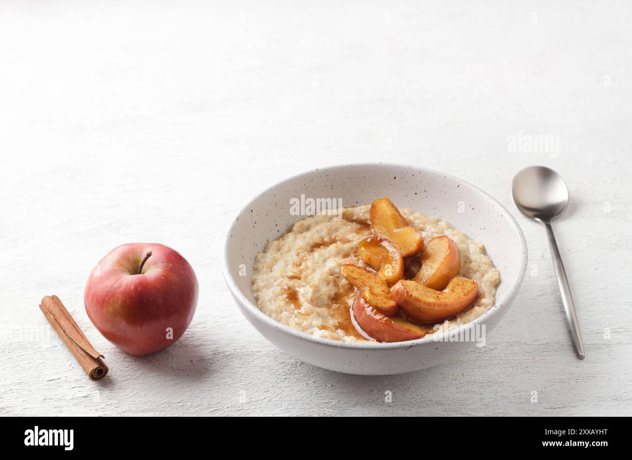 Bouillie d'avoine sucrée avec tranches de pomme cuites au four, cannelle et sauce caramel dans un bol gris sur fond clair Banque D'Images