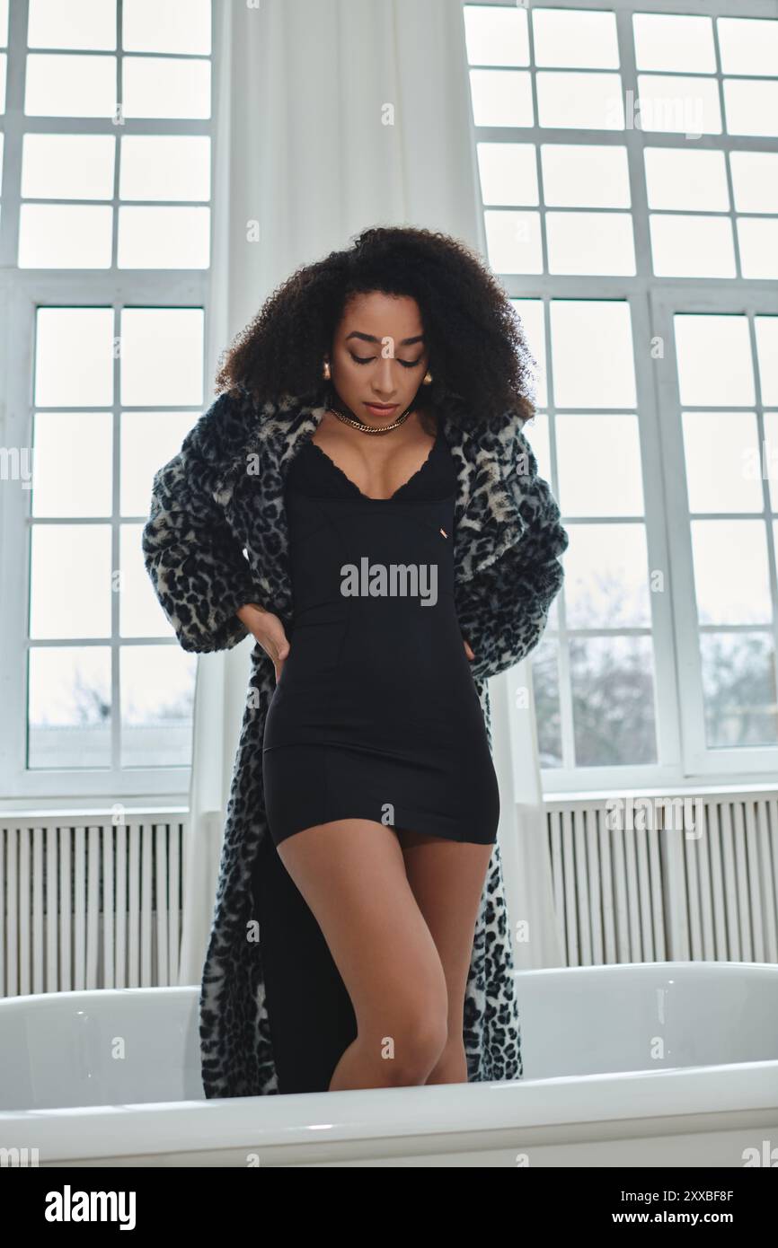 Une femme afro-américaine élégante dans une robe noire et un manteau léopard pose dans un cadre de studio, créant une image chic et moderne. Banque D'Images