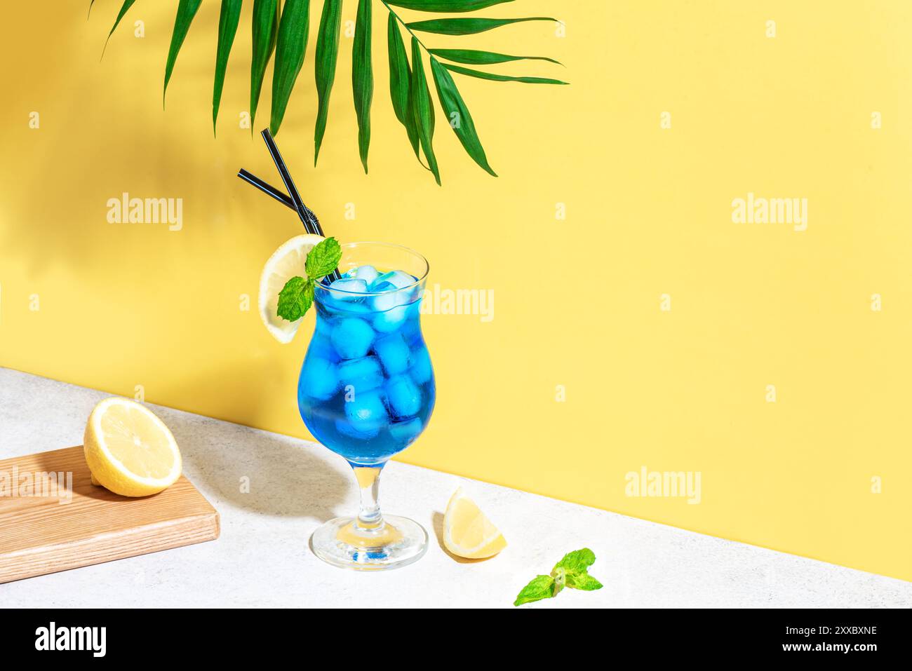 Cocktail d'été Blue Lagoon à la menthe et au citron sur fond jaune vif avec feuille de palmier, espace copie. Concept de fête de plage créative à la mode. Cocktail Banque D'Images